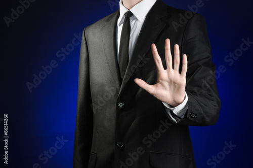 Businessman and gesture topic: a man in a black suit and white shirt showing gestures with hands palm against the dark blue isolated background in studio