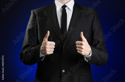 Businessman and gesture topic: a man in a black suit and white shirt showing hand gestures a thumbs-up on a dark blue background in studio isolated