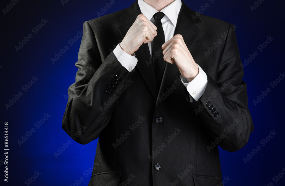 Businessman and gesture topic: a man in a black suit and white shirt holding his fists in front of him on a dark blue background in studio isolated