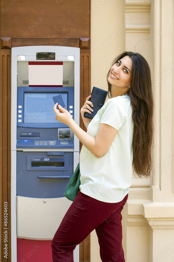 Young woman in jeans short using an automated teller machine Young woman in jeans short using an automated teller machine