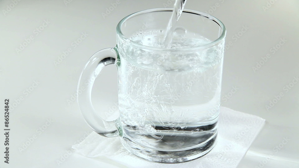 Mineral Water is Poured Into a Glass Mug on a White Background Mineral Water is Poured Into a Glass Mug on a White Background