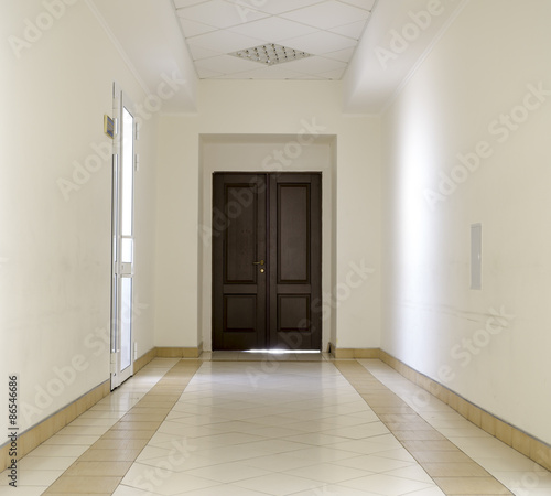 White hallway with marble floor and brown door in hospital