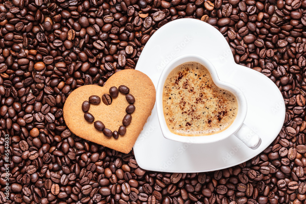 Heart shaped cup and cookie on coffee beans background Heart shaped cup and cookie on coffee beans background