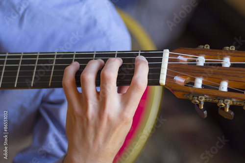 Acoustic guitar's fretboard and young male's hand