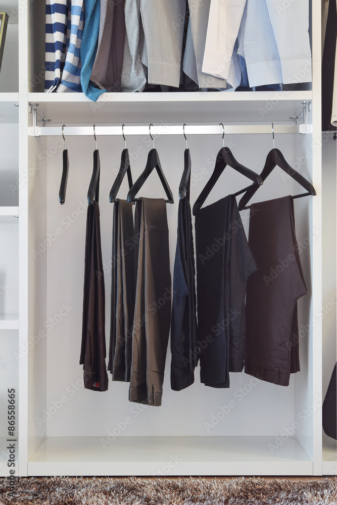 modern closet with row of pants hanging in white wardrobe