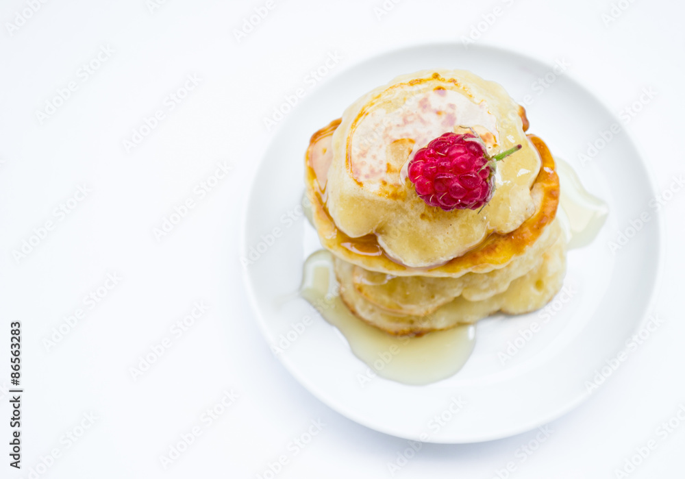 Stack of pancakes on plate, raspberries and honey, top view