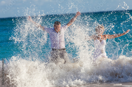 Young wedding couple have a fun in ocean waves © vladmilkov