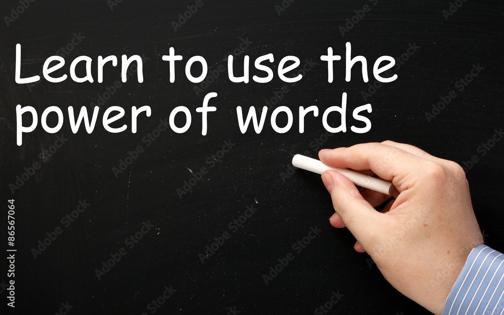 Male hand wearing a business shirt writing the phrase Learn to use the Power of Words in white text on a blackboard Male hand wearing a business shirt writing the phrase Learn to use the Power of Words in white text on a blackboard