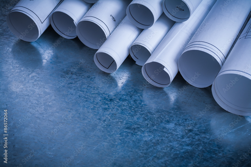 Fototapeta premium Rolls of white construction plans on scratched metallic backgrou