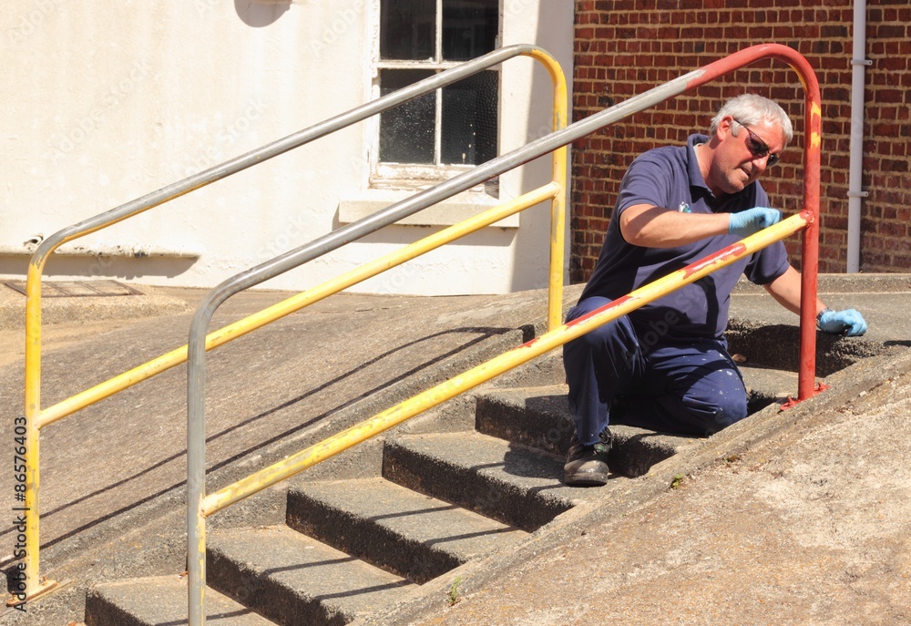 A painter painting handrails along a walkway with concrete steps A painter painting handrails along a walkway with concrete steps