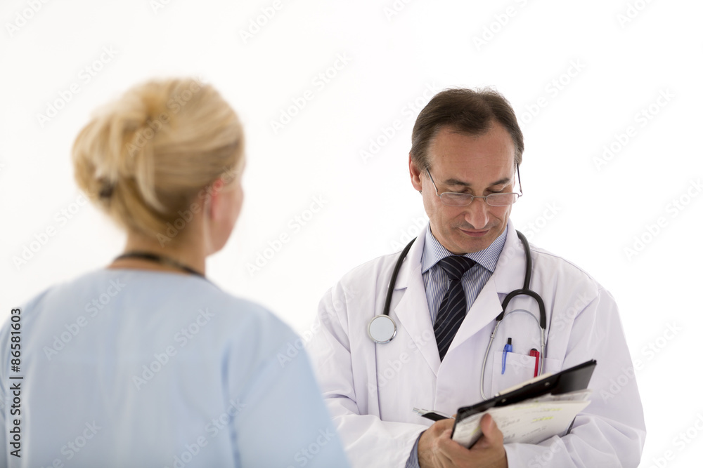 Male doctor with glasses writing something on his clipboard giving instructions to a blond female colleague, back turned. Indoors Male doctor with glasses writing something on his clipboard giving instructions to a blond female colleague, back turned. Indoors