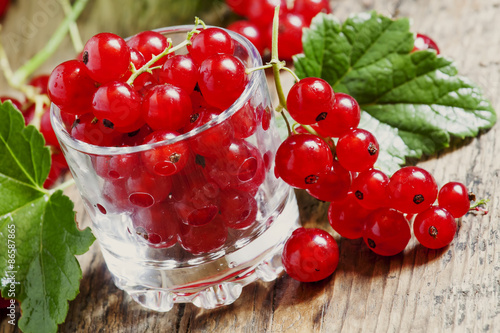 Fresh red currants with leaves in glass on a wooden table, selec photo