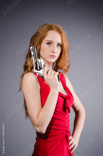 Pretty young girl in red dress with gun isolated on white