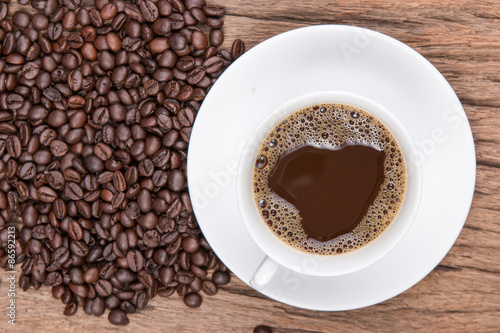 Cup of black coffee and coffee beans on wooden background