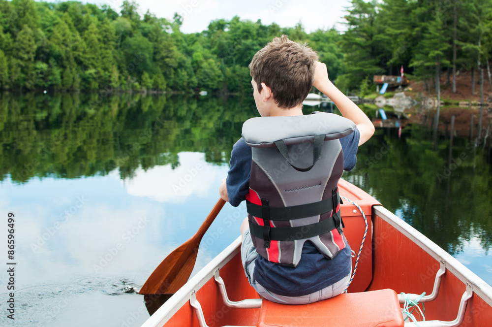 young boy paddling in a calm lake in the front of a canoe