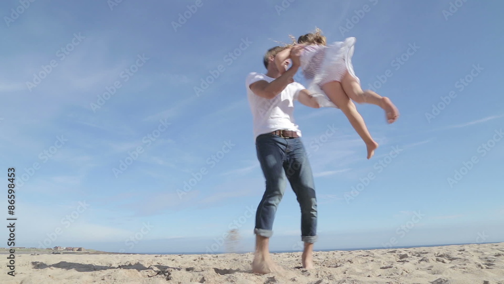 Father picks up and spins his daughter round on the beach before putting her down and running to the side with her. Father picks up and spins his daughter round on the beach before putting her down and running to the side with her.