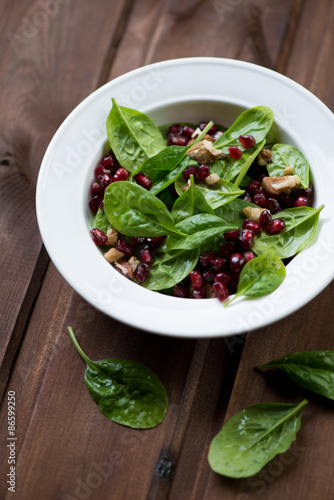Glass plate with spinach, pomegranate and walnuts salad, closeup