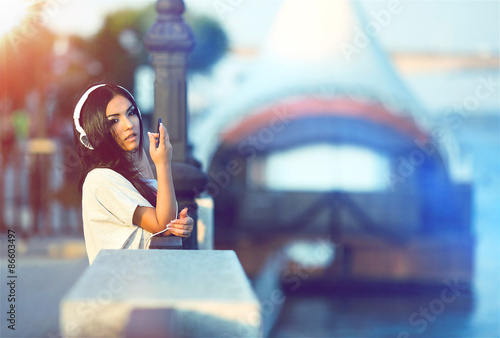 Young brunette girl alone listening to the music in a headphones on the city background