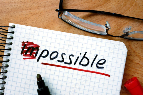 Notepad with converting the word impossible to possible on office wooden table.