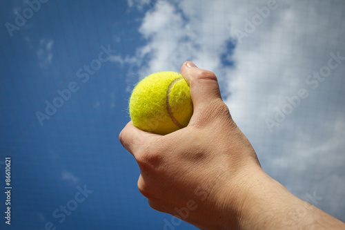 Hand holding tennis ball up to the sky
