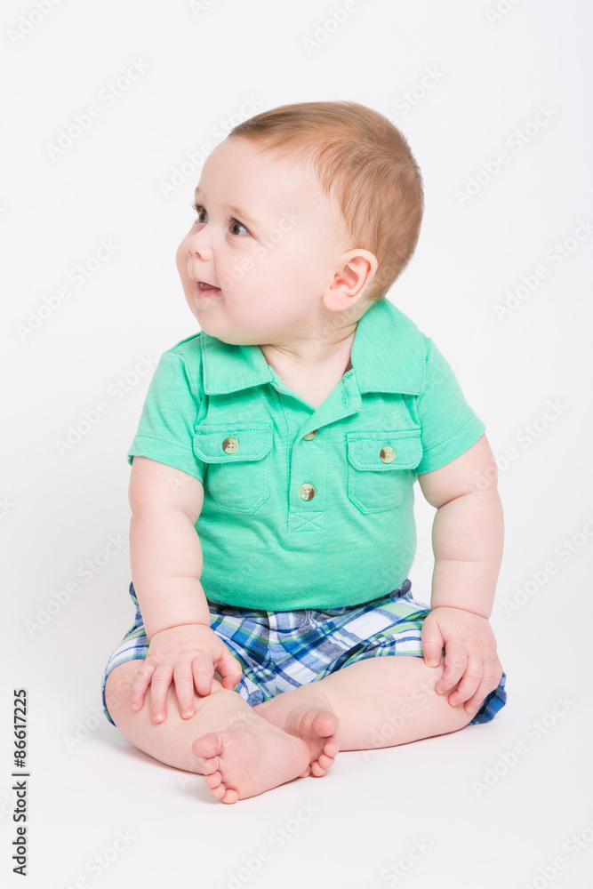 8 month year old baby sits on a white background looking off camera. dressed in a cute green polo shirt and blue plaid shorts. 8 month year old baby sits on a white background looking off camera. dressed in a cute green polo shirt and blue plaid shorts.