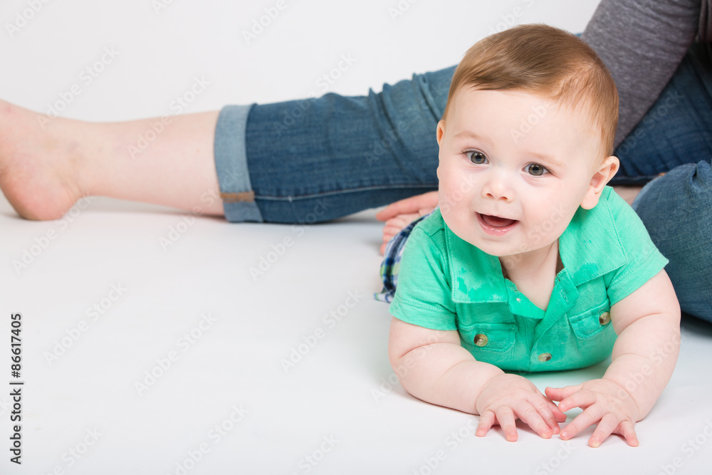 8 month year old baby lays on his stomach looking towards camera, while mom is sitting in background. dressed in a cute green polo shirt and blue plaid shorts. 8 month year old baby lays on his stomach looking towards camera, while mom is sitting in background. dressed in a cute green polo shirt and blue plaid shorts.
