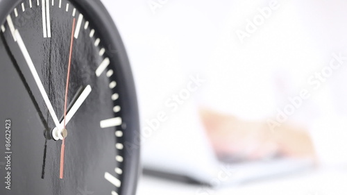 Close up of running clock with business man working on laptop in the back - working time or deadline concept