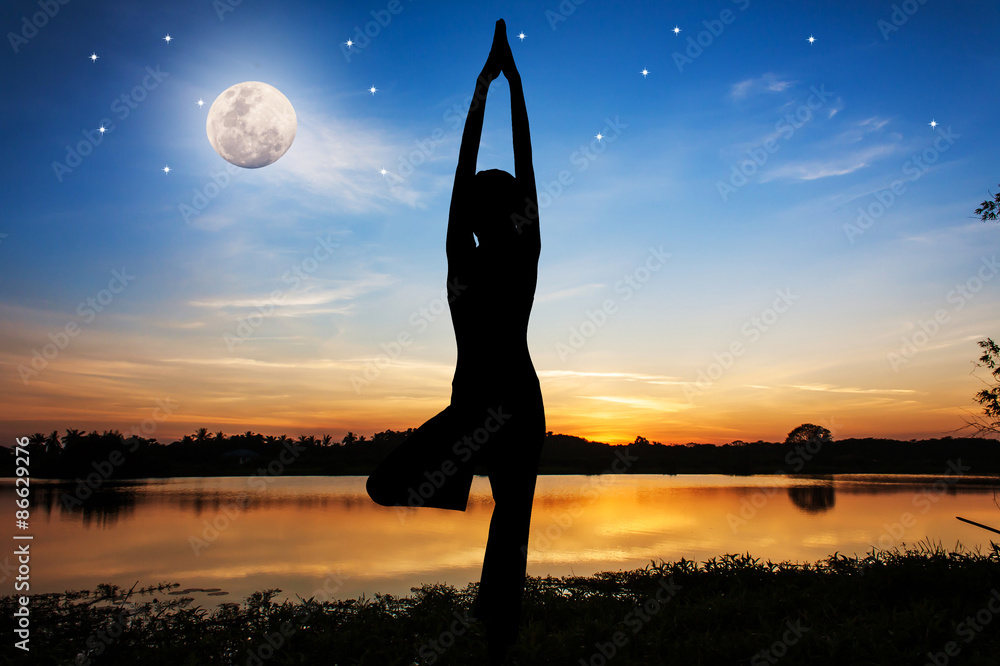 Silhouette young woman practicing yoga at river on night full moon background