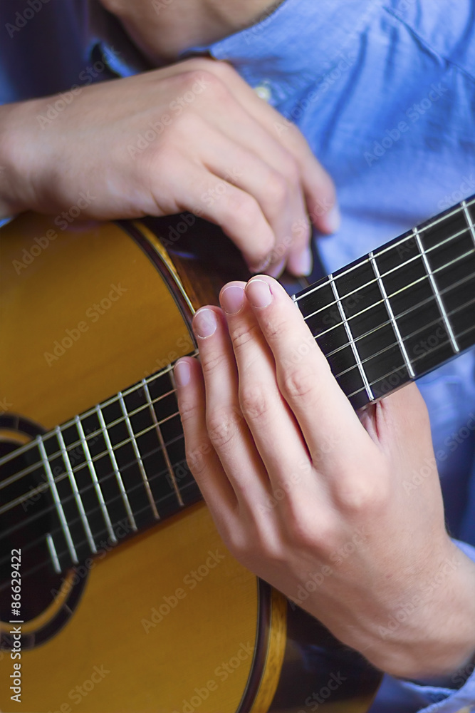 Acoustic guitar's fretboard and young male's hands