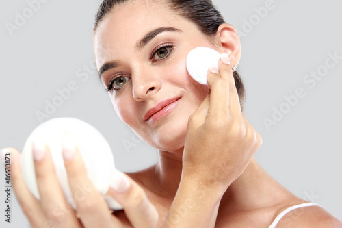 cheerful young model smiling while holding a compact powder and