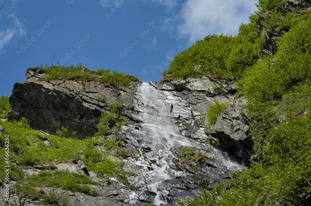 High waterfall in Carpathians mountains under blue sky. High waterfall in Carpathians mountains under blue sky.