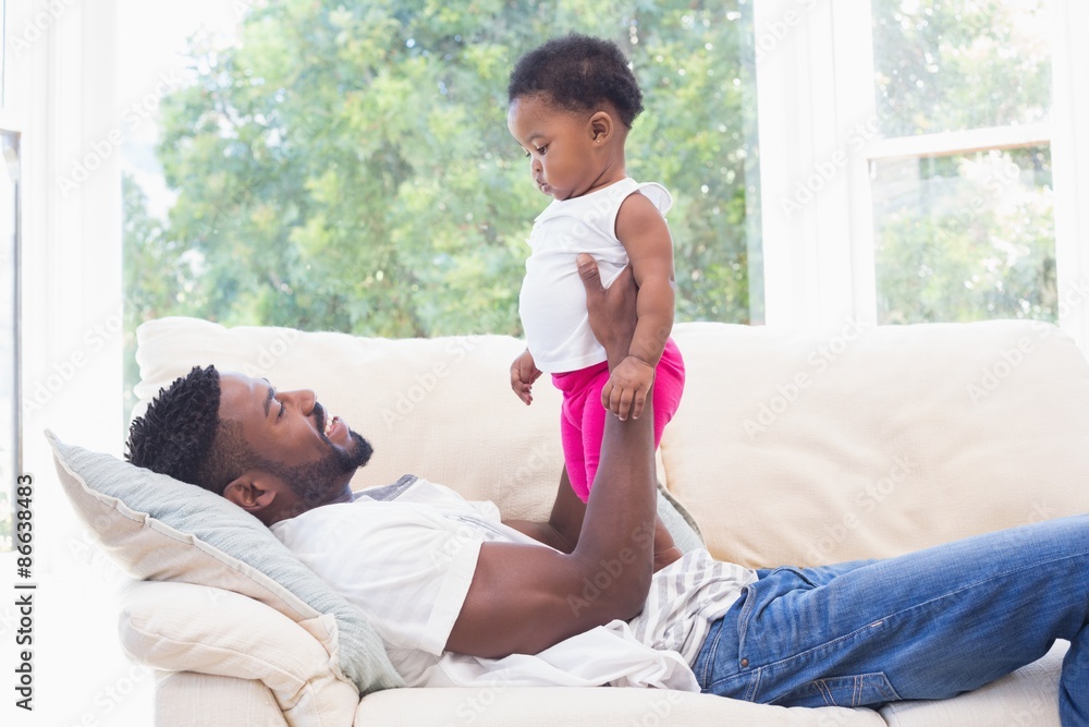 Happy father with baby girl on couch - obrazy, fototapety, plakaty 