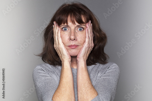 portrait of anxious beautiful 50's woman under shock with both hands on face for fear and stress photo