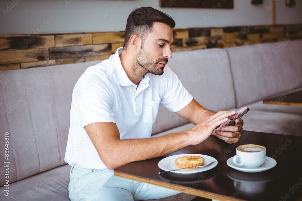 Young man having cup of coffee and pastry while texting in a cafe Young man having cup of coffee and pastry while texting in a cafe