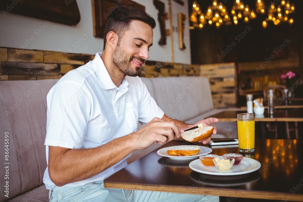 Young man spreading butter on a toast at the cafe