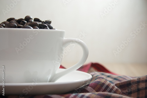 Close up coffee beans in white cup on wooden table and tablecloth plaid red brown with copy space use for background, vintage effect