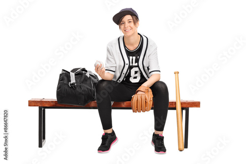 Female athlete holding a baseball seated on a bench