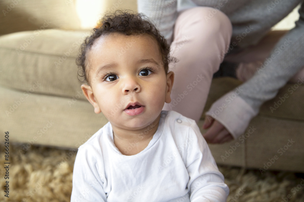 Baby boy sitting on the floor of his front room with his mother sitting on the sofa behind him. Baby boy sitting on the floor of his front room with his mother sitting on the sofa behind him.