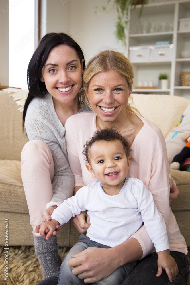 Female couple sit together with their son in their home and all smile for the camera