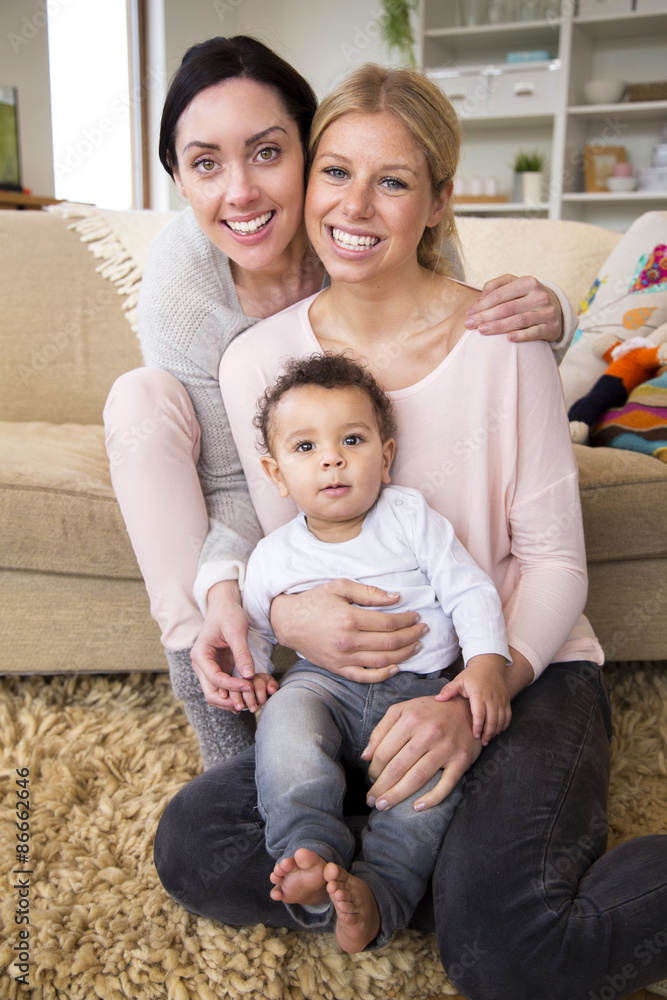Female couple sit together with their son in their home and smile for the camera