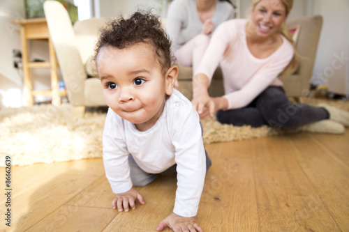 Foto Female couple watch proudly as their baby son crawls along the floor
