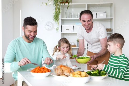 Same sex male couple having dinner with their son and daughter in their home.
