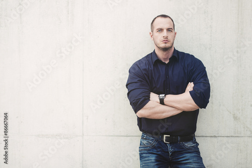 Man posing outside, leaning on a wall.