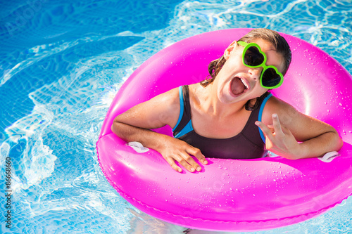 happy teenager playing on a pink buoy in a pool with sunglasses photo