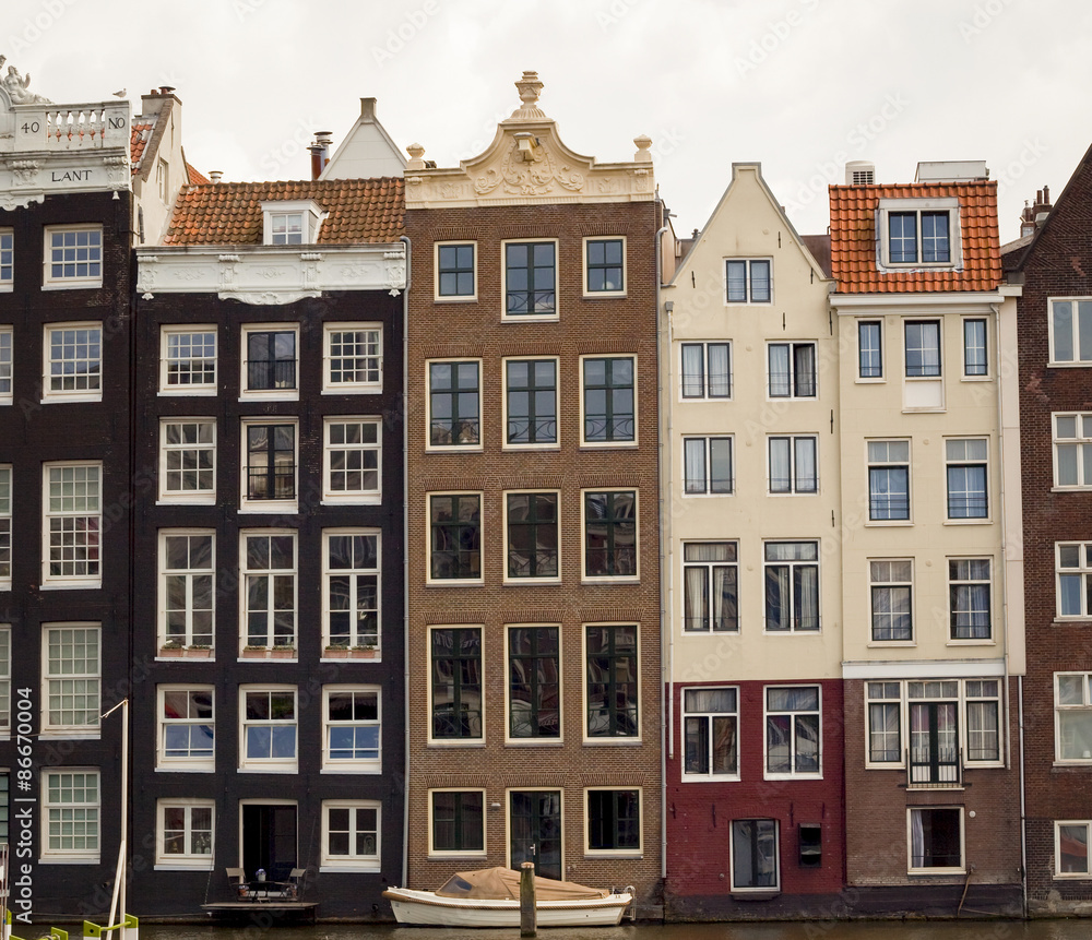 Row of typical crooked building facades lining canal with boat in Amsterdam