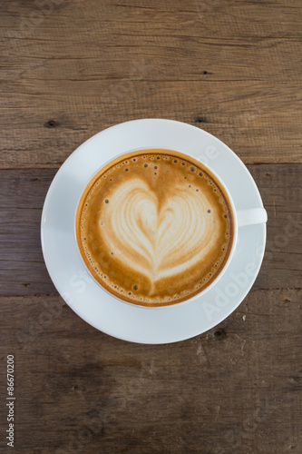 A cup of coffee with heart pattern in a white cup on wooden background