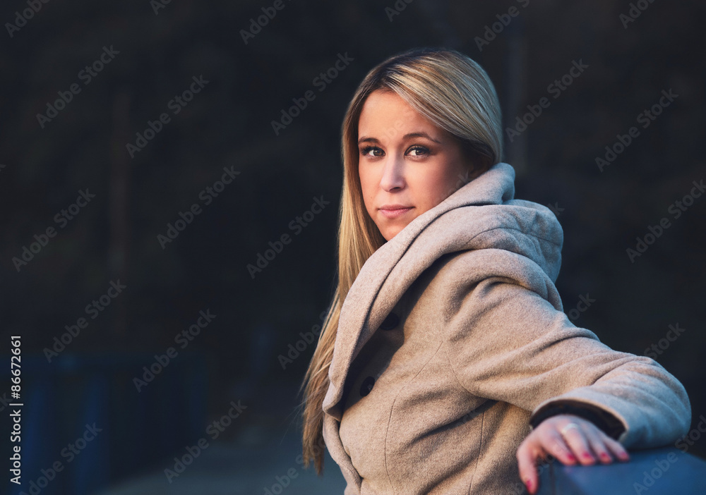 Portrait of a fashionable stylish girl in a coat. Looking and smiling while standing against the fence. Shallow depth of field Outdoors, lifestyle. Portrait of a fashionable stylish girl in a coat. Looking and smiling while standing against the fence. Shallow depth of field Outdoors, lifestyle.