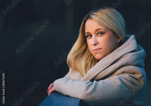 Portrait of a fashionable stylish girl in a coat. Looking and smiling while standing against the fence. Shallow depth of field Outdoors, lifestyle.