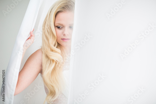 Gorgeous young woman/bride wearing a lovely dress, in a window,