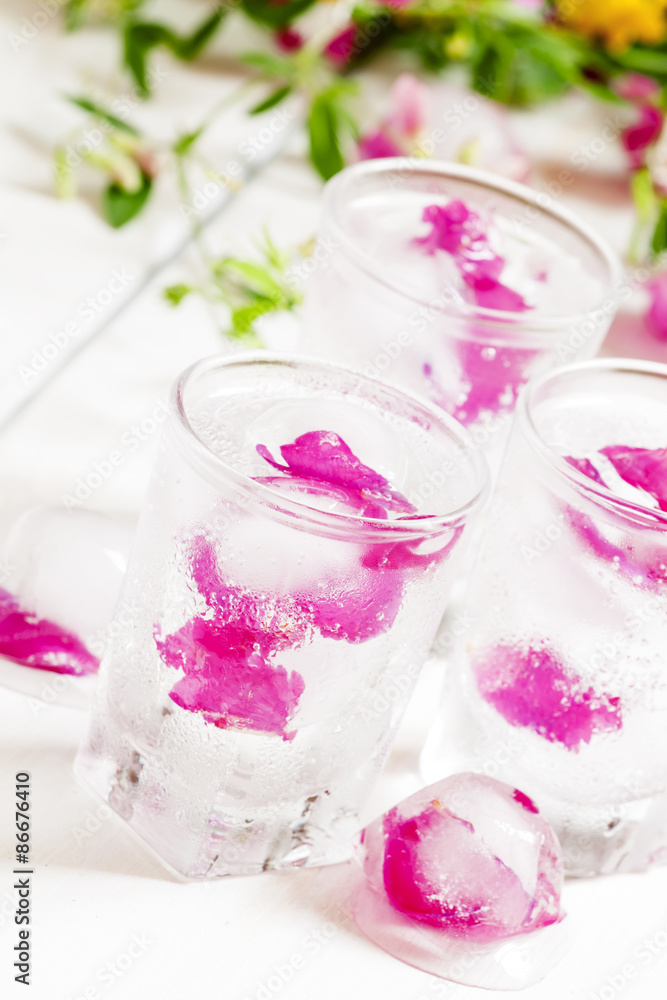 Fresh sparkling beverage with ice with rose petals on white wood Fresh sparkling beverage with ice with rose petals on white wood